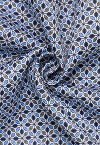 Tessuto di cotone con un motivo vorticoso, caratterizzato da design floreali geometrici blu, verdi e neri su uno sfondo bianco.