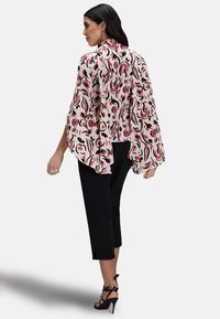 Luftig, långärmad blus i beige med ett djärvt röd och svart blommönster. Kombinerad med svarta korta byxor och svarta sandaler med remmar.