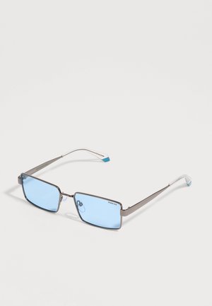Gafas de sol rectangulares con montura plateada, lentes azul claro y extremos transparentes en las varillas sobre un fondo blanco.