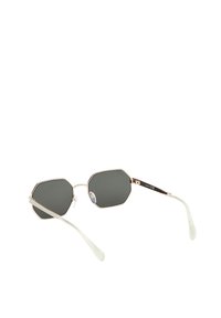 Gafas de sol octogonales con lentes oscuros, montura de metal plateado y puntas de las varillas en verde translúcido. Cuenta con un sutil logotipo en el brazo.
