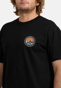 T-shirt in cotone nero con un logo grafico sul petto, caratterizzato da colori tra cui rosso, blu e giallo. Collo a giro e maniche corte.