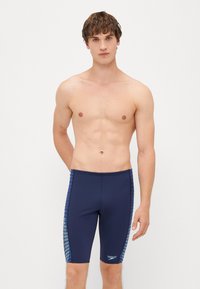 Shorts de bain navy en tissu extensible, avec des accents bleus sur les côtés et une coupe ajustée. Pas de motifs ni de logos visibles.