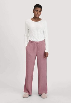 Weißes, geripptes Langarmtop kombiniert mit weiten, strukturierten Blush-Hosen. Das Model trägt hellgraue Hausschuhe. Einfaches, lässiges Design.