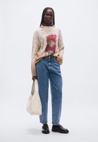 Kootud džemper leopardimustriga, millel on suur tiigri graafika punases mütsis. Sobitatud siniste kõrge vöökohaga teksade ja mustade kingadega.