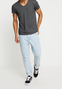 Dark gray v-neck t-shirt, light blue baggy jeans, black and white sneakers, casual fit, smooth texture, minimal branding on the shirt.