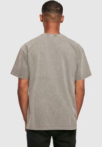 Camiseta de algodón gris con mangas cortas, escote redondo y textura desvanecida. Sin gráficos ni adornos visibles, diseño simple.