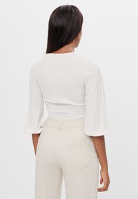 White textured crop top with smocked waist and wide sleeves, paired with light beige high-waisted pants featuring back pockets.