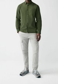 Groen textuur overhemd met knopen, lichtgrijze cargobroek met zakken en grijze sport schoenen met witte veters.