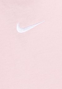 Logo Nike w białym haftowanym na jasnoróżowej, prążkowanej tkaninie. Gładka tekstura z miękkim, jednolitym kolorem.
