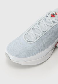 Light blue athletic shoe with a mesh upper, flat laces, and red accents. Features a rounded toe and a white rubber sole with textured patterns.
