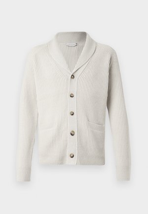 Cardigan crème com uma textura canelada, gola xale, bolsos frontais e botões castanhos. Design simples com mangas longas e um corte reto.