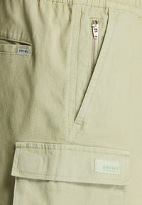 Svetlozelené cargo šortky s vreckom na zips a predným náprsným vreckom so šitým štítkom. Tkanina má štruktúrovaný povrch.