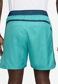 Turquoise athletic shorts with a textured, diamond pattern. Features a navy elastic waistband and side pockets. Lightweight fabric.
