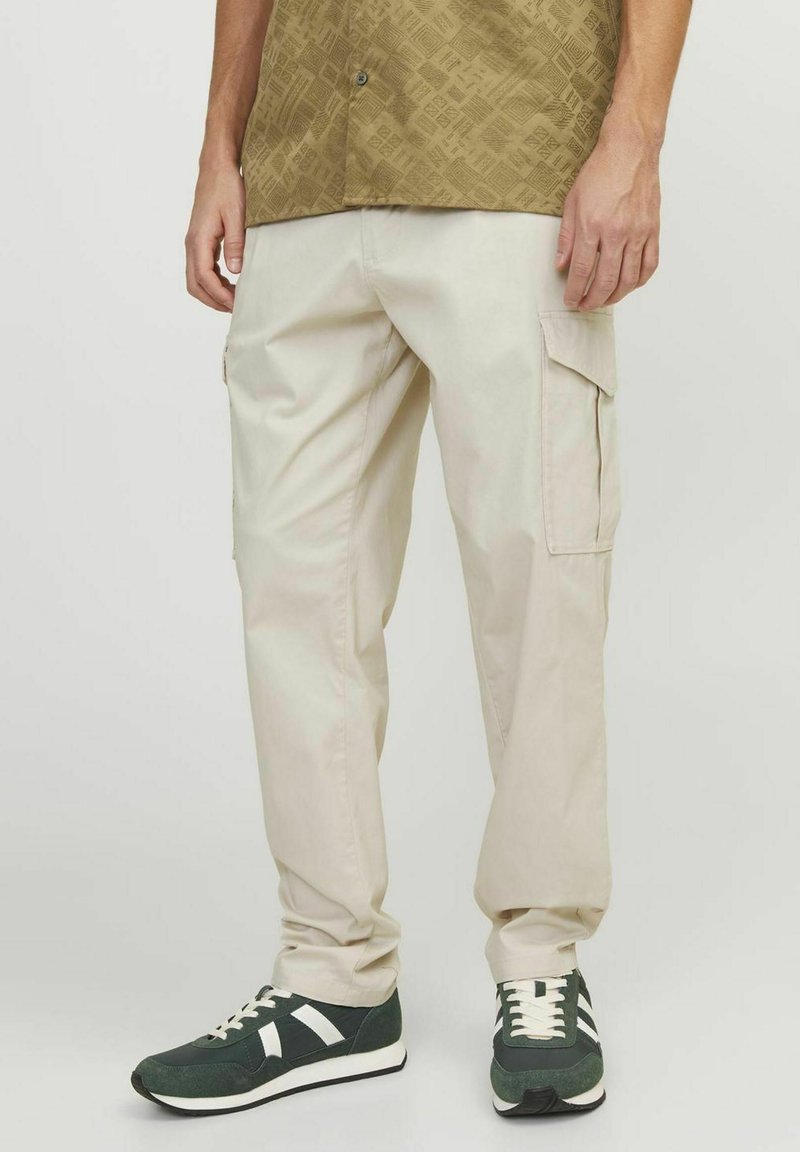 Pantalones cargo beige con bolsillos laterales, con un diseño de pierna recta. Llevados con zapatillas verdes que tienen acentos blancos.