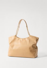 Δερμάτινη τσάντα χρώματος ταχίνι με απλή υφή, μαλακή μορφή και χρυσές αλυσίδες για τις λαβές. Κομψός, μινιμαλιστικός σχεδιασμός χωρίς ορατό υλικό.