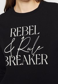 Felpa nera con grande testo bianco: "REBEL & Rule BREAKER." Design con collo rotondo e una texture di tessuto liscia e opaca.