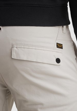 Beige pants pocket with buttoned flap and PME Legend label, worn with black ribbed fabric top.