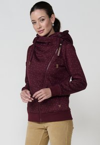 Bordo zip-up dukserica s cowl vratom, teksturiranim materijalom, kapicama i drvenim detaljima. Ima dijagonalni zatvarač i uske manžete.