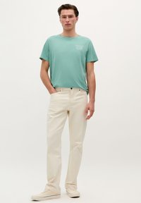 Turquoise t-shirt met korte mouwen en een borstprint, gecombineerd met crèmekleurige skinny jeans en lichtgekleurde sneakers. Eenvoudig ontwerp, soepele textuur.