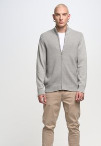 Grijze rits cardigan met een gestructureerd breipatroon, geribbelde manchetten en zoom, gecombineerd met beige broek. Beschikt over een subtiel, modern ontwerp.