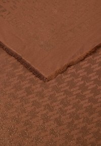 Brun vævet stof med et struktureret houndstooth-mønster og subtil glans. Kanterne har en frynset finish, der fremhæver stoffets tekstur.