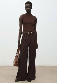 Top sans manches en tricot marron associé à un pantalon large marron à rayures taille haute. Accessoirisé avec un sac à main marron et des chaussures noires.