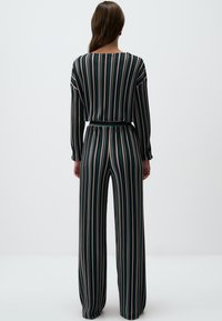 Zwart-groene gestreepte jumpsuit met lange mouwen, wijde pijpen, stof die op de taille is aangetrokken, met een zachte textuur en verticale lijnen.