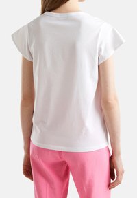 White cotton t-shirt with short cap sleeves, round neckline, and a straight cut hem, worn with pink relaxed-fit pants.
