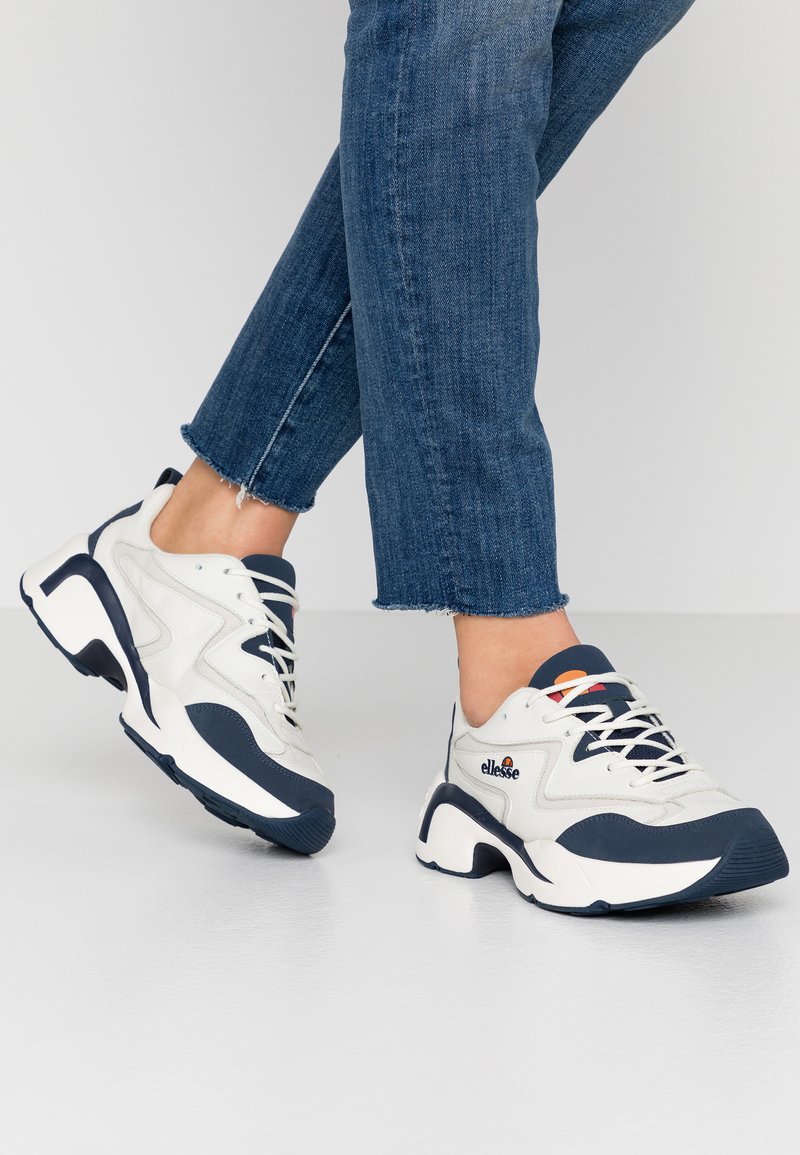 Sneaker chunky bianche e blu navy con pannelli in rete e sintetici, presentano una suola testurizzata e un logo sobrio sul lato.