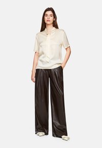Cremefarbige Satinbluse mit kurzen Ärmeln und Bindekragen, kombiniert mit high-waisted schwarzen Leder-Hosen im weiten Schnitt. Elegant und lässig geschnitten.