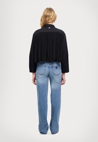 Camicia nera corta con design sul retro a pieghe, abbinata a jeans a vita alta di un azzurro chiaro. I pantaloni sono leggermente larghi e scoloriti.