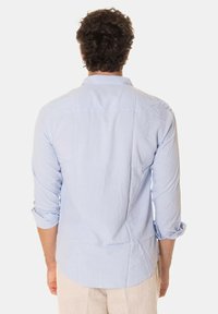 Camicia a maniche lunghe blu chiaro in cotone. Presenta uno yoke posteriore e maniche arrotolate con polsini a bottoni. Tessuto liscio, orlo dritto.