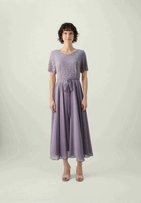 Vestido lavanda com corpete rendado, mangas curtas e cintura laçada. A saia fluida tem uma textura suave, criando uma silhueta delicada.