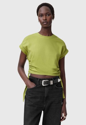 Lyhythihainen oliivinvihreä crop-top, jossa on kerättyä sivudetaileita, yhdistettynä korkeavyötäröisiin mustiin farkkuihin ja mustaan vyöhön, jossa on hopeiset yksityiskohdat.
