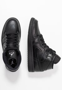 Mustat nahkakengät korkealla varsilla, joissa on strukturoitu pinta, pyöreä kärki, mustat nauhat ja kumipohja. Sisältää Air Jordan -merkinnän kielen kohdalla.