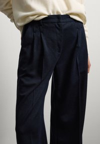 Navy weit geschnittene Hosen mit strukturiertem Finish, gefaltetem Vorderteil und elastischem Bund, kombiniert mit einem cremefarbenen Pullover.