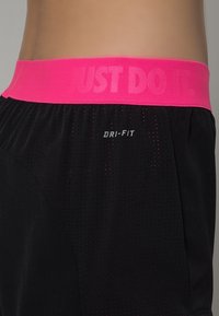 Gros plan sur un short de sport noir avec une ceinture rose affichant les inscriptions "JUST DO IT." et "DRI-FIT" sur le côté.