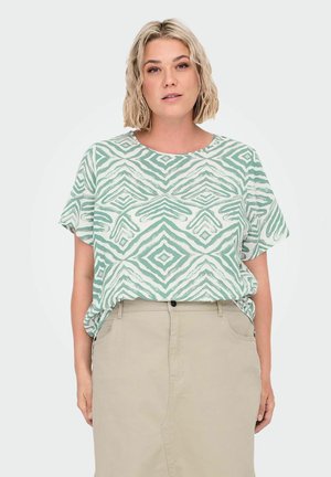 T-shirt à manches courtes avec un motif géométrique vert menthe et blanc. Le tissu semble doux avec une coupe décontractée, associé à une jupe beige.