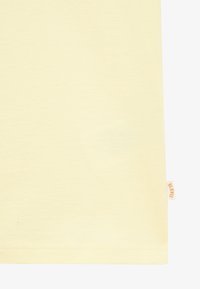 Tissu de couleur crème avec une petite étiquette beige sur le côté droit portant la mention « BLK WLS », montrant l'ourlet d'un vêtement.