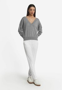 Grauer, lässig geschnittener V-Ausschnitt-Pullover mit geripptem Saum, kombiniert mit weißen, schmal zulaufenden Hosen und weißen Sneakers mit hellbraunen Sohlen. Minimalistisches Design.
