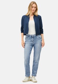 Veste de bombardier navy avec des poignets élastiques, débardeur blanc, jean droit bleu clair et baskets blanches. Tenue décontractée avec un minimalisme dans les détails.
