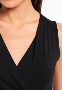 Top nero senza maniche con scollo a V, realizzato in un tessuto liscio con sottili dettagli drappeggiati sulle spalle e una silhouette aderente.