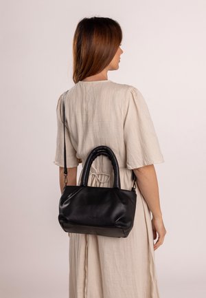 Czarna skórzana torba o luźnym fasonie, z plecioną rączką i odczepianym paskiem na ramię, wyeksponowana na neutralnym tle.