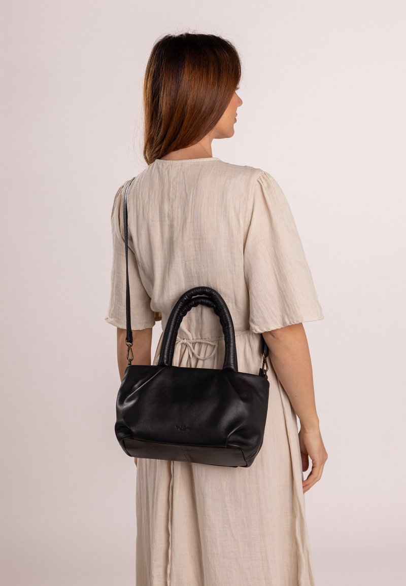 Czarna skórzana torba o luźnym fasonie, z plecioną rączką i odczepianym paskiem na ramię, wyeksponowana na neutralnym tle.