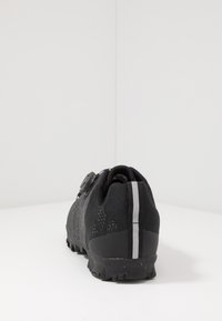 Černá sportovn í obuv s texturovaným pleteným svrškem, kruhovým ovladačem pro nastavení velikosti a pevným podpatkem s reflexní šedou pruhou.