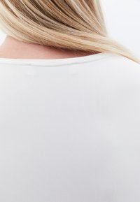 Weißes, glattes Stoffoberteil mit rundem Ausschnitt. Die Rückseite hat eine subtile Naht und ist auf eine enganliegende Passform abgestimmt, die die Textur zur Geltung bringt.