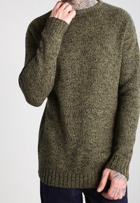 Mörkgrön stickad tröja med ett strukturerat mönster, ribbade ärmmuddar och nederkant. Tillverkad av mjukt fabric, med en avslappnad passform och rund halsringning.