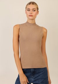 Beige ärmelloses Oberteil mit hohem Hals, geripptem Muster, figurbetontem Design und weichem Strickstoff. Kombiniert mit dunkelblauen, verzierten Denim-Shorts.