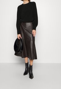 Černá blůza s dlouhým rukávem a žebrovanými detaily, kombinovaná s tmavě hnědými koženými midi sukněmi. Outfit doplňují černé podpatekové boty do kotníku a černá kabelka.