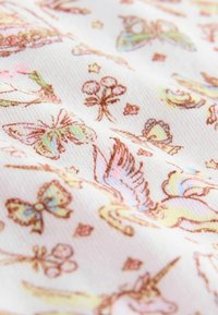 Tissu blanc avec des illustrations pastel de papillons, de fleurs, d'étoiles et d'une licorne dans un motif féerique.